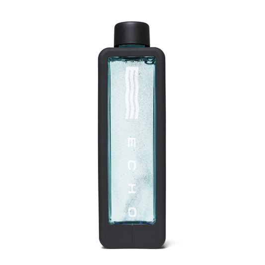 A tall rectangular water bottle with a matte black frame and cap, featuring a clear front panel filled with light blue water and vertical white branding text.