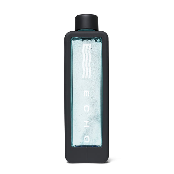 A tall rectangular water bottle with a matte black frame and cap, featuring a clear front panel filled with light blue water and vertical white branding text.